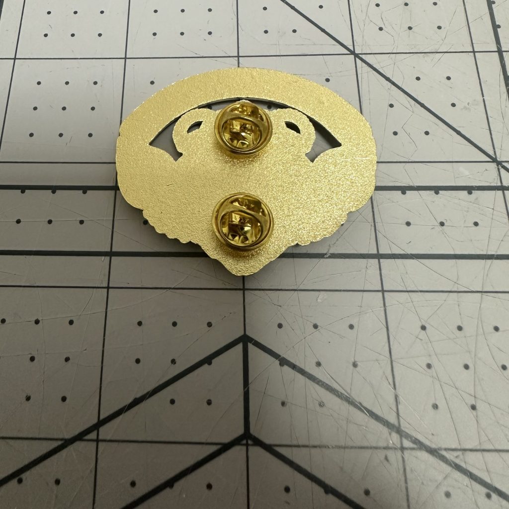 Reverse of a gold-plated enamel pin showing two butterfly clutches